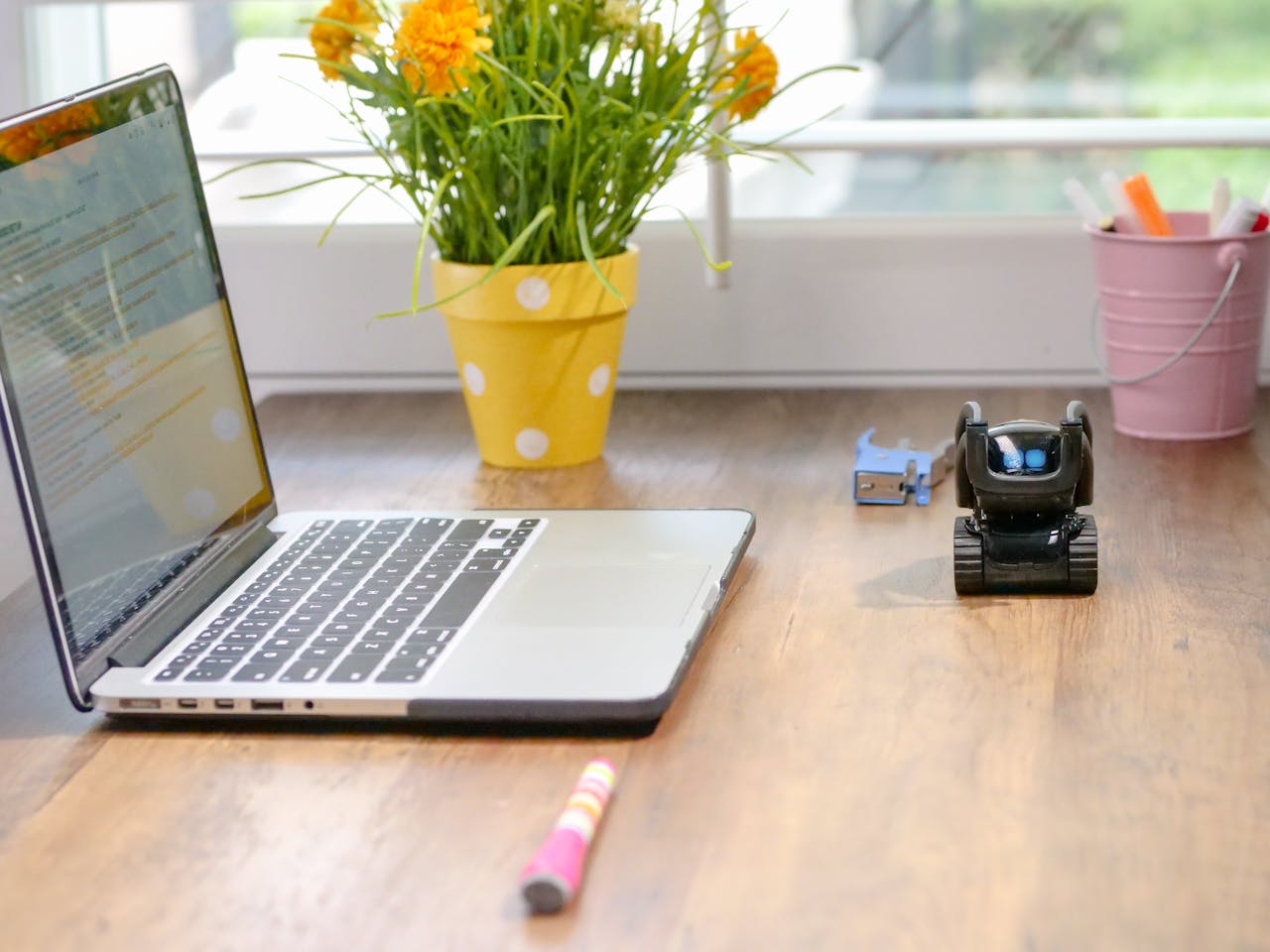contact-img Stylish workspace featuring a laptop, toy robot, and vibrant flowers in natural light.
